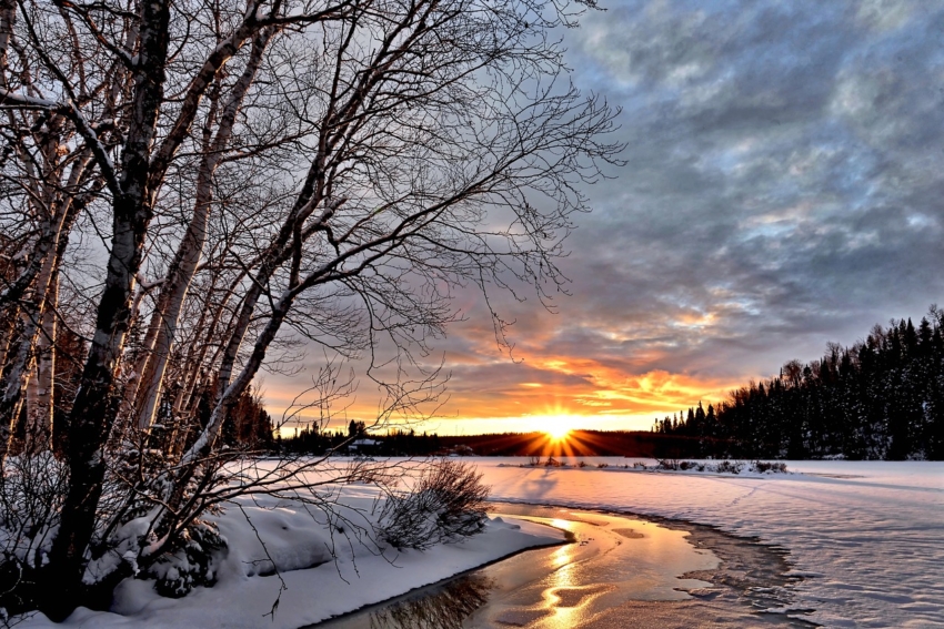 winterliche Flusslandschaft mit Sonnenuntergang und kahlen Bäumen